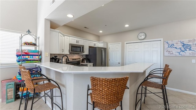 kitchen featuring a breakfast bar area, stainless steel appliances, a peninsula, white cabinets, and light countertops