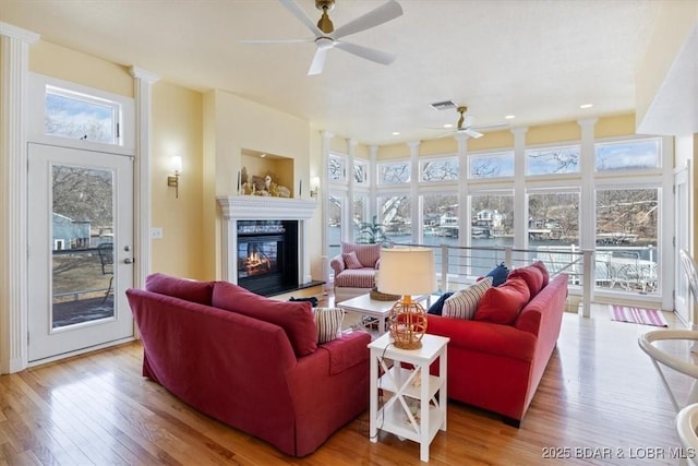 living room with ceiling fan, a glass covered fireplace, wood finished floors, and visible vents