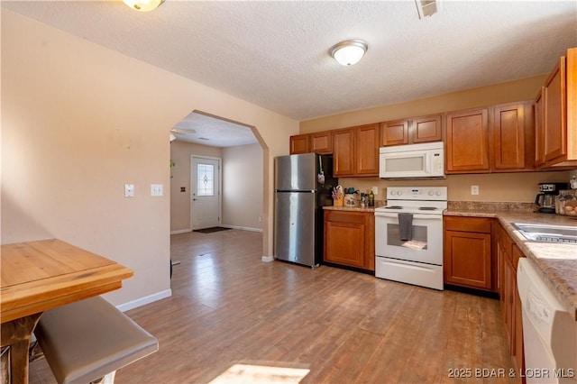 kitchen with white appliances, arched walkways, brown cabinets, light countertops, and light wood-type flooring