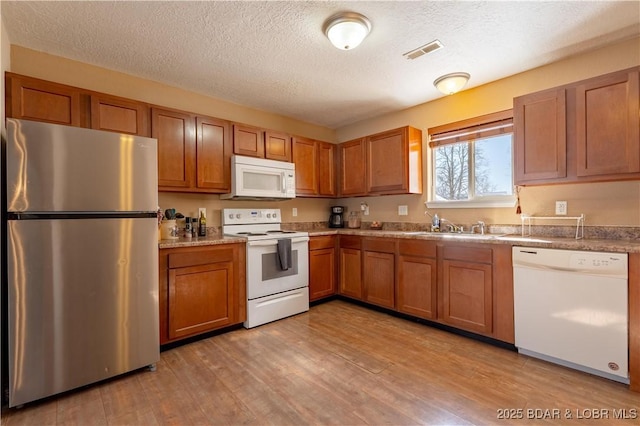 kitchen with white appliances, a sink, visible vents, light wood-type flooring, and brown cabinetry