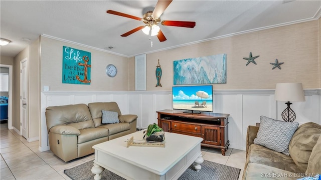 living area with light tile patterned floors, a decorative wall, ornamental molding, wainscoting, and ceiling fan