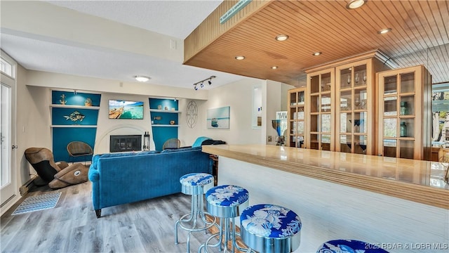 kitchen with built in shelves, wood finished floors, wood ceiling, open floor plan, and a glass covered fireplace