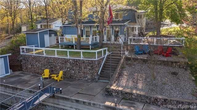 rear view of house featuring a deck, a patio, a storage shed, an outdoor structure, and stairs