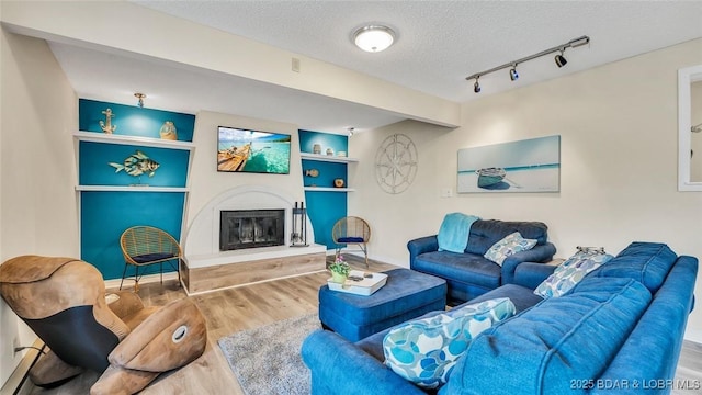 living room featuring built in features, a glass covered fireplace, wood finished floors, a textured ceiling, and track lighting