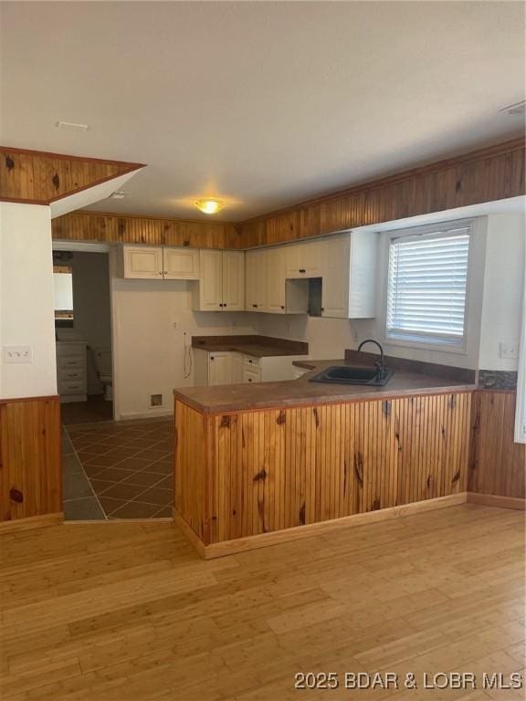 kitchen with a peninsula, a sink, light wood-style flooring, and wooden walls