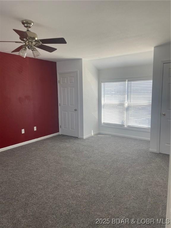 spare room with a ceiling fan, dark colored carpet, and baseboards