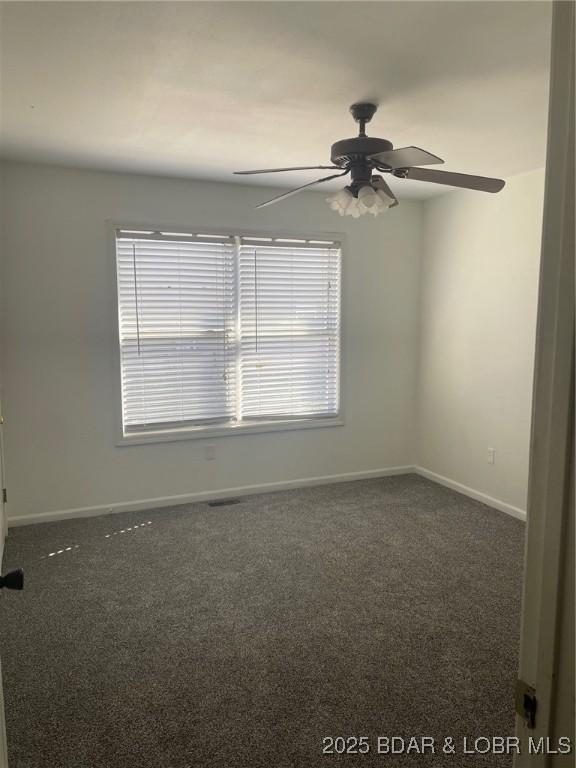 unfurnished room featuring baseboards, dark colored carpet, and a ceiling fan