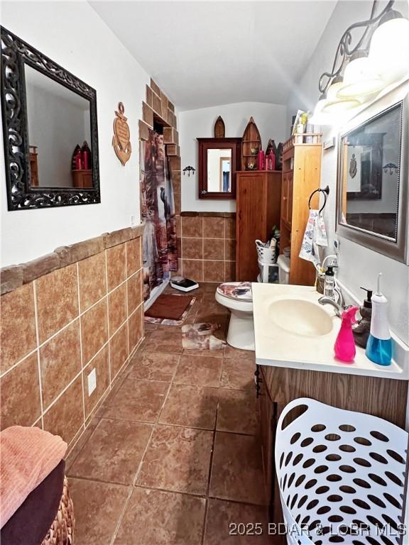 bathroom featuring wainscoting, toilet, tile patterned flooring, vanity, and tile walls