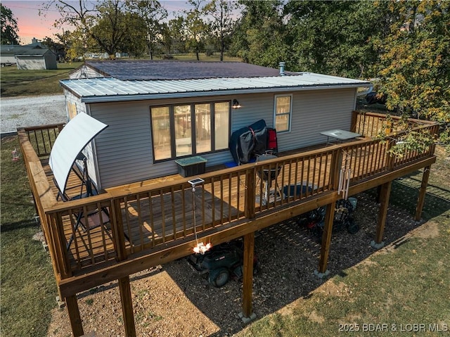 back of house at dusk featuring metal roof and a wooden deck