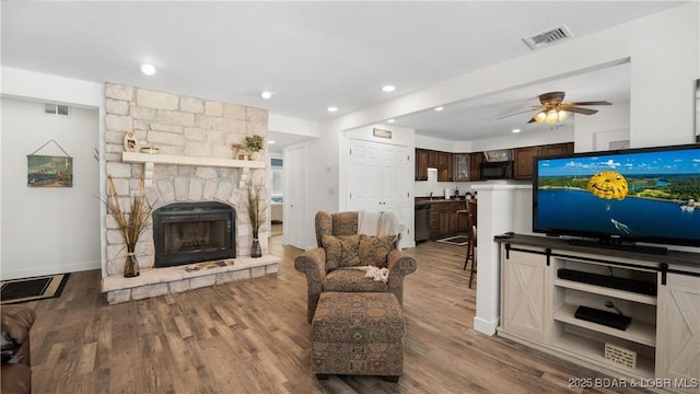 living room with a ceiling fan, a fireplace, visible vents, and wood finished floors