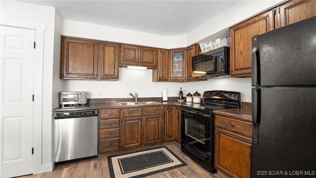 kitchen with light wood-type flooring, dark countertops, a sink, and black appliances