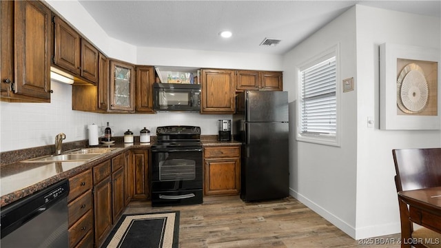 kitchen with visible vents, wood finished floors, a sink, black appliances, and backsplash