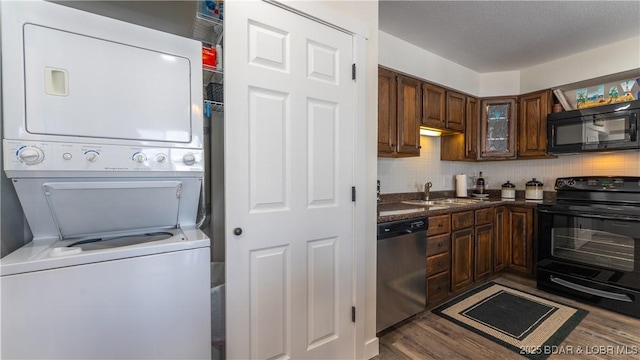 kitchen featuring a sink, stacked washer / drying machine, backsplash, black appliances, and dark countertops