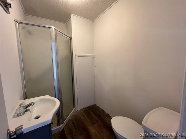 full bathroom with a textured ceiling, toilet, wood finished floors, a sink, and a shower stall