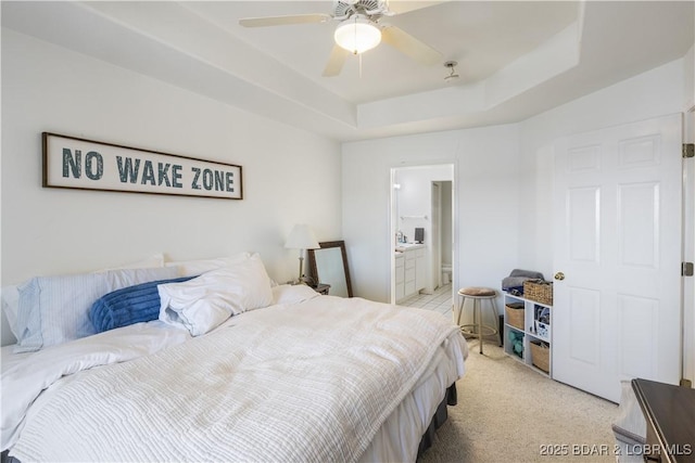 bedroom featuring ensuite bath, a tray ceiling, a ceiling fan, and light colored carpet