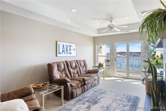 carpeted living area featuring a tray ceiling, a water view, a ceiling fan, and recessed lighting