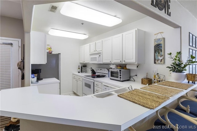 kitchen with a peninsula, white appliances, a breakfast bar area, and light countertops