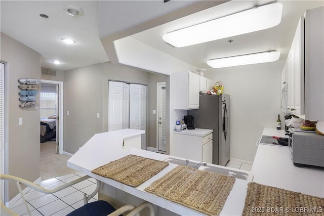 kitchen featuring a breakfast bar area, a peninsula, visible vents, white cabinetry, and light countertops