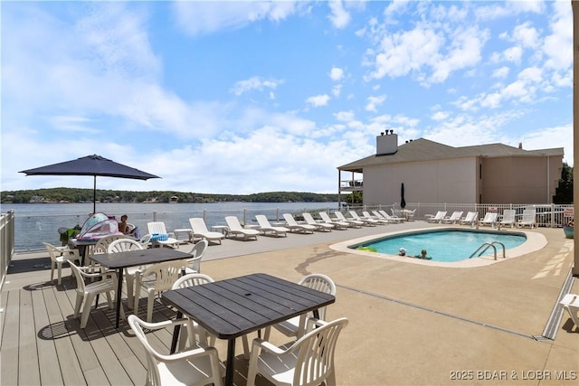 pool featuring a patio area, a water view, and fence