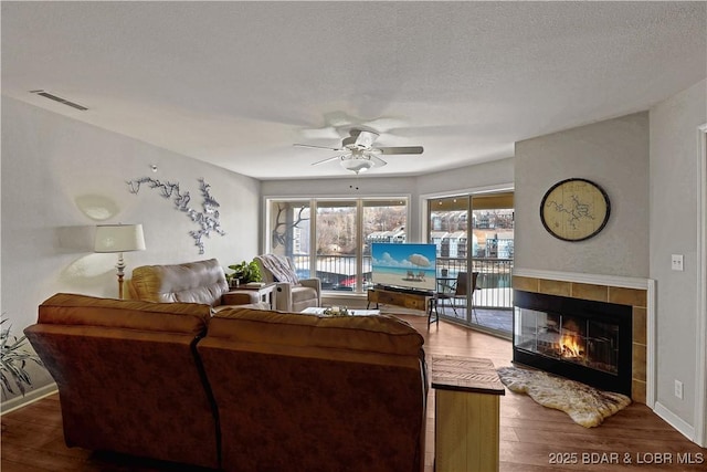 living area featuring ceiling fan, a fireplace, wood finished floors, and visible vents