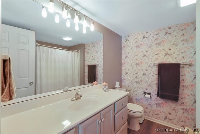 full bath featuring wallpapered walls, baseboards, toilet, wood finished floors, and vanity