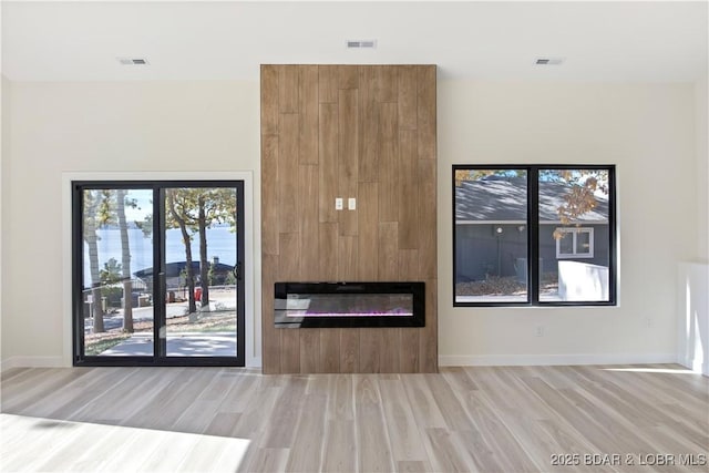 unfurnished living room with a water view, a fireplace, visible vents, baseboards, and light wood-type flooring