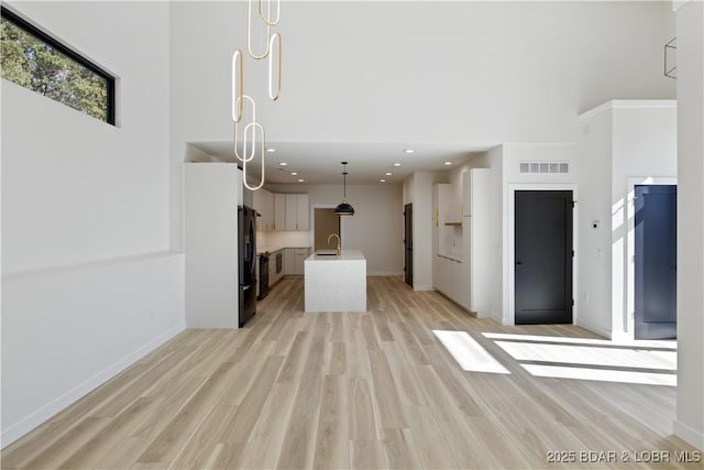 unfurnished living room with light wood finished floors, visible vents, a high ceiling, a sink, and baseboards