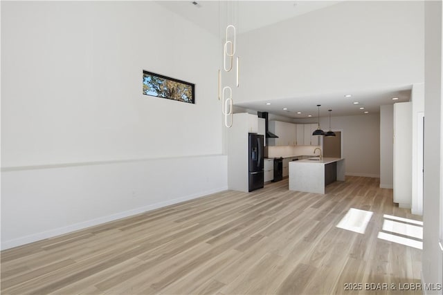 unfurnished living room with recessed lighting, baseboards, a towering ceiling, and light wood finished floors