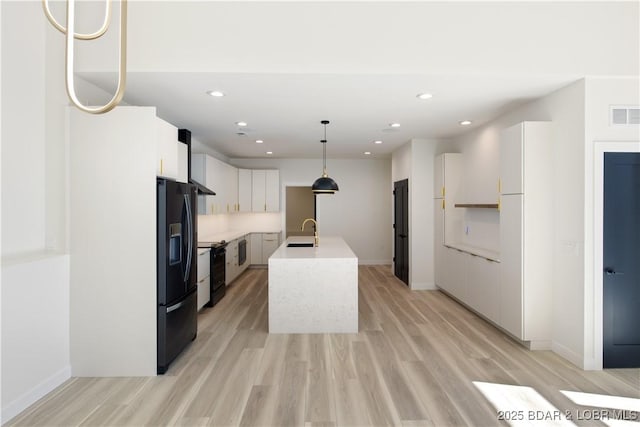 kitchen with white cabinetry, light countertops, black appliances, an island with sink, and decorative light fixtures