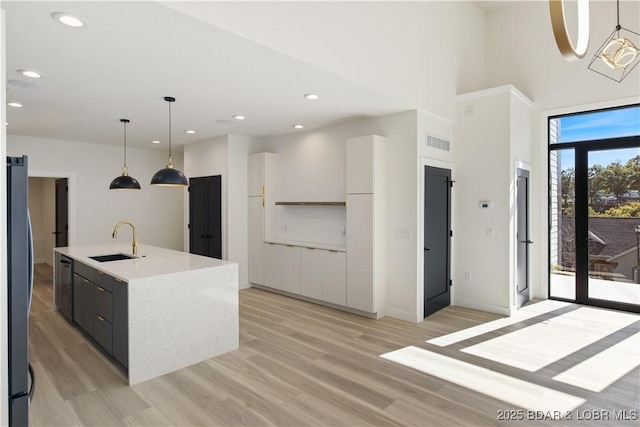 kitchen with pendant lighting, stainless steel appliances, light countertops, a kitchen island with sink, and a sink