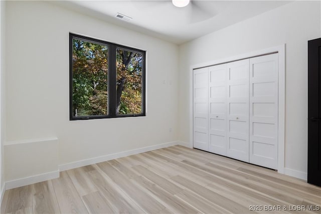 unfurnished bedroom with light wood finished floors, visible vents, baseboards, and a closet