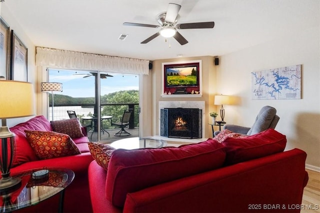 living room with ceiling fan, a premium fireplace, wood finished floors, and visible vents