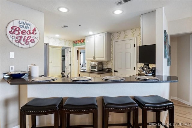 kitchen featuring dark countertops, white cabinetry, a peninsula, and wallpapered walls