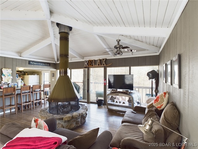 living area featuring lofted ceiling with beams, hardwood / wood-style flooring, wooden walls, and a ceiling fan