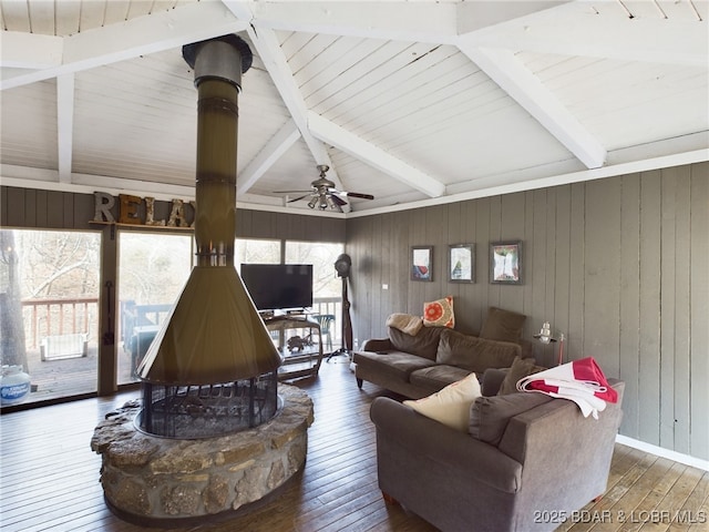 living area featuring vaulted ceiling with beams, a healthy amount of sunlight, a wood stove, and hardwood / wood-style flooring