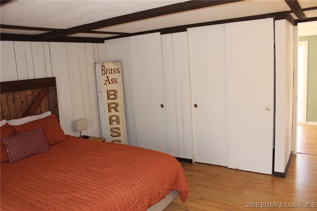 bedroom with beamed ceiling, a closet, and light wood-style flooring