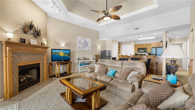 living area featuring a tray ceiling, visible vents, light carpet, ceiling fan, and a tile fireplace