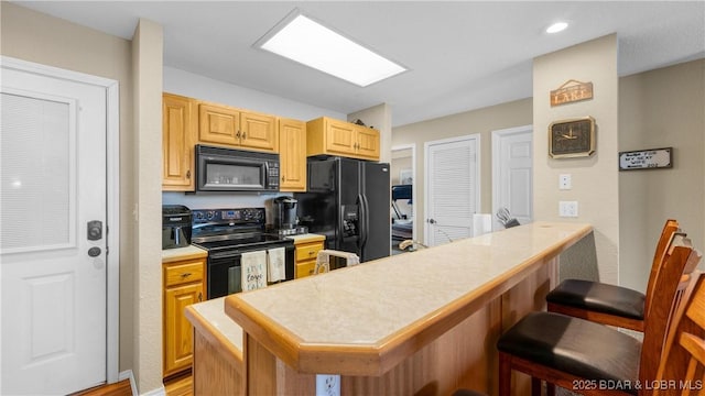 kitchen with a breakfast bar area, recessed lighting, light countertops, a peninsula, and black appliances