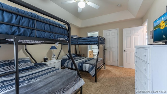 carpeted bedroom with a raised ceiling and a ceiling fan