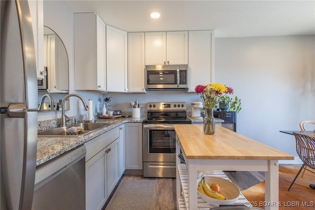 kitchen featuring recessed lighting, butcher block counters, appliances with stainless steel finishes, white cabinetry, and a sink