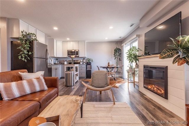 living room with dark wood-type flooring, a glass covered fireplace, visible vents, and recessed lighting