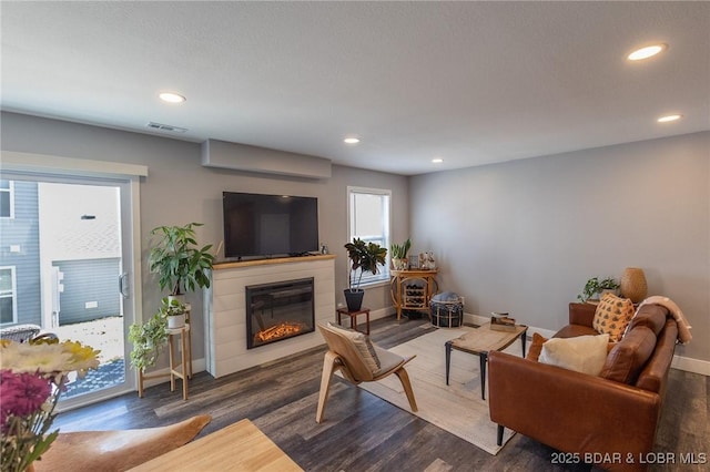 living room featuring a glass covered fireplace, visible vents, baseboards, and wood finished floors