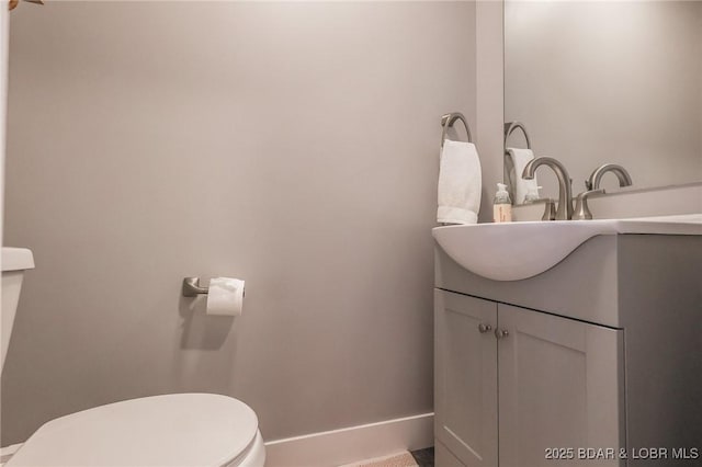 half bath with baseboards, vanity, and toilet