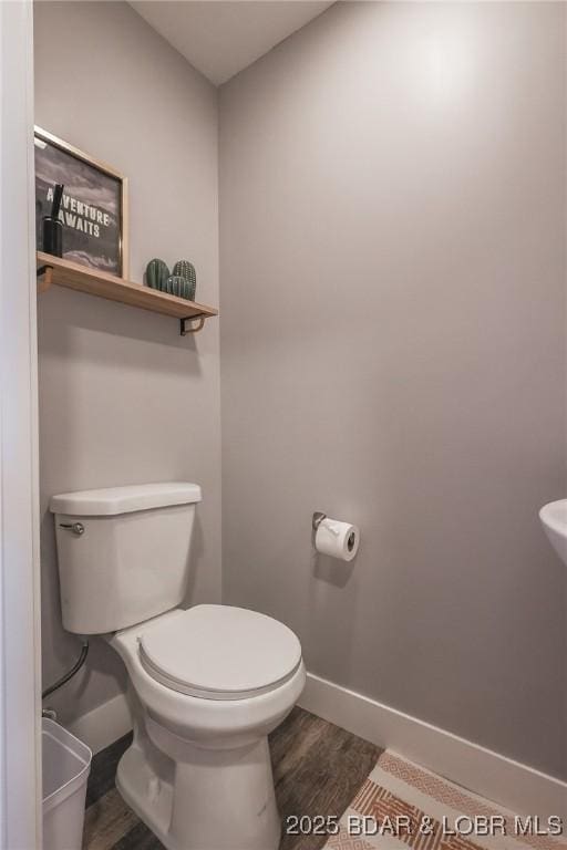 half bathroom with wood finished floors, toilet, and baseboards