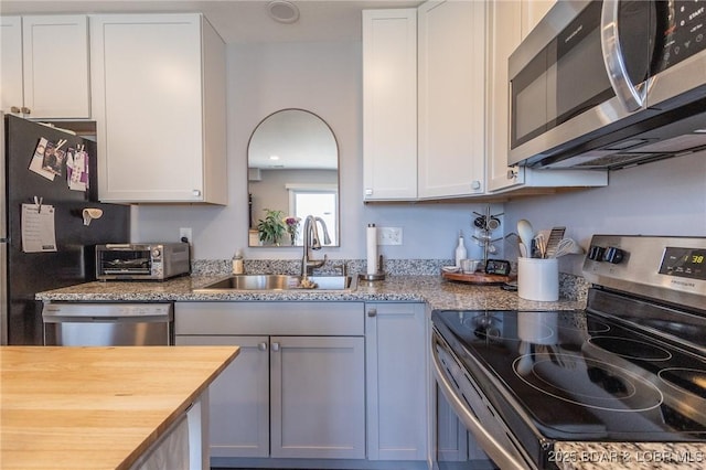 kitchen featuring a toaster, white cabinets, butcher block counters, stainless steel appliances, and a sink