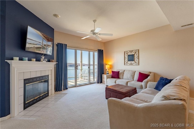 living room featuring ceiling fan, visible vents, carpet flooring, and a tile fireplace