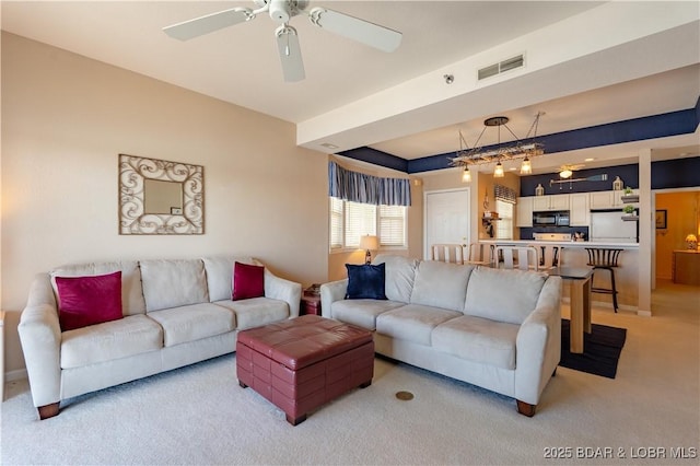 living room featuring a ceiling fan, a raised ceiling, visible vents, and light carpet