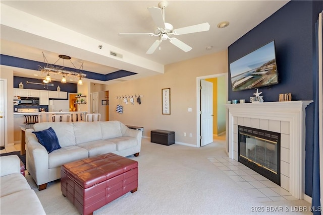 living area featuring light carpet, baseboards, visible vents, a ceiling fan, and a tiled fireplace