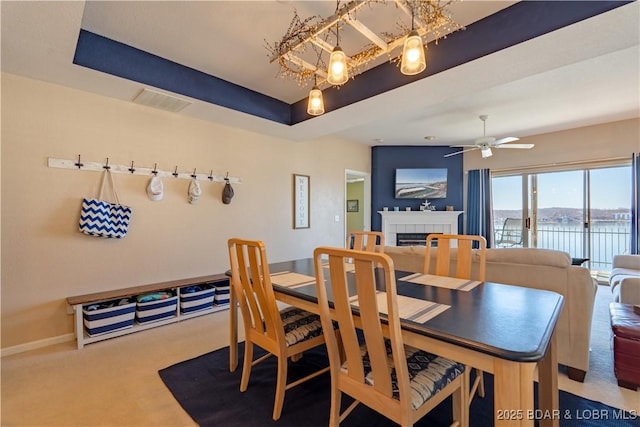 carpeted dining space featuring a tile fireplace, visible vents, ceiling fan, and baseboards