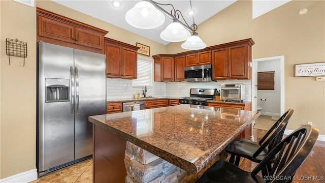 kitchen featuring backsplash, appliances with stainless steel finishes, a kitchen island, baseboards, and hanging light fixtures